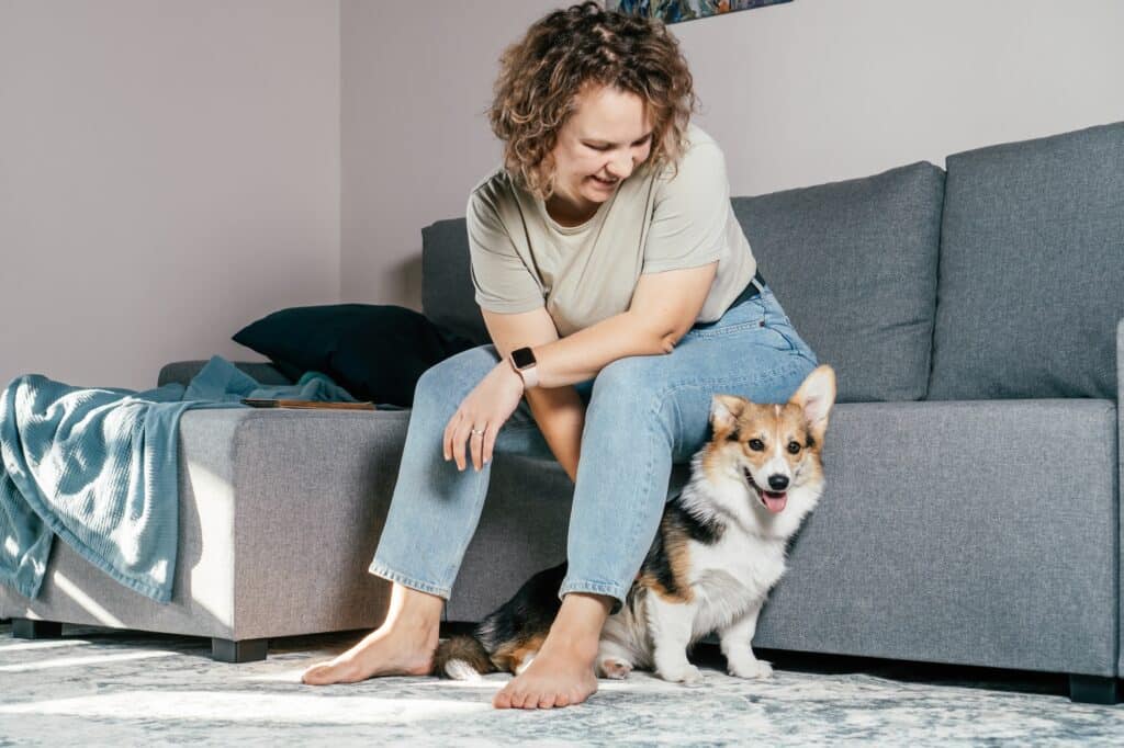 Curly cheerful woman with dog corgi sitting, relaxing and playing on floor at home. Active fur pet